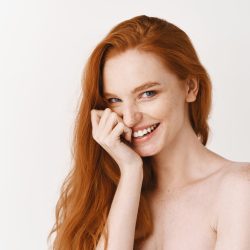 Beauty and skincare. Close-up of happy redhead woman with pale perfect skin, laughing and showing white teeth, standing naked on studio background.